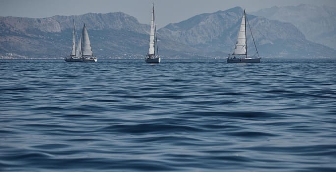 The race of sailboats, a regatta, reflection of sails on water, Intense competition, number of boat is on aft boats, island with windmills are on background