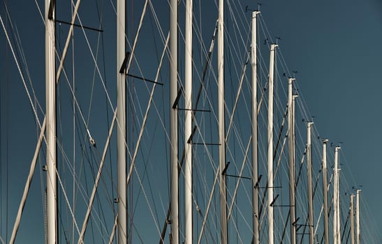 The number of masts of sailboats with the blue sky on a background, a sail regatta, reflection of masts on water, ropes and aluminum