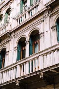 Close-ups of buildings in Venice, Italy. Incredibly beautiful stone facades of buildings in Venetian style - stone arched windows with columns and balconies, with small details of sculptures