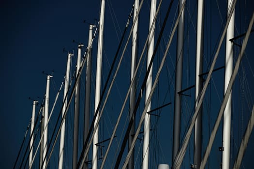 The number of masts of sailboats with the blue sky on a background, a sail regatta, reflection of masts on water, ropes and aluminum