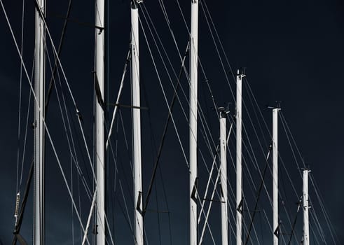 The number of masts of sailboats with the blue sky on a background, a sail regatta, reflection of masts on water, ropes and aluminum