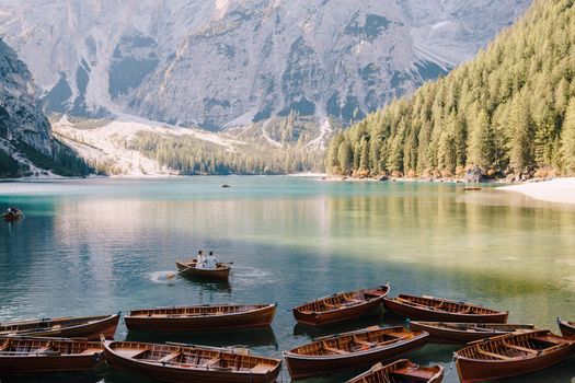 Wedding couple swim in a wooden boat on Lago di Braies in Italy. Newlyweds in Europe, at Braies Lake, in the Dolomites. The groom rows with oars, the bride sits opposite him.