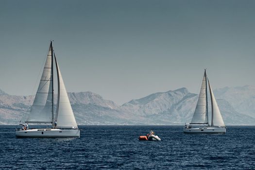 The rubber boat of organizers of a regatta with the judge and balloon of orange color, The race of sailboats, Intense competition, island is on background