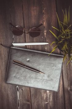 notepad glasses and a flower in a pot on a wooden table top view pen office. High quality photo