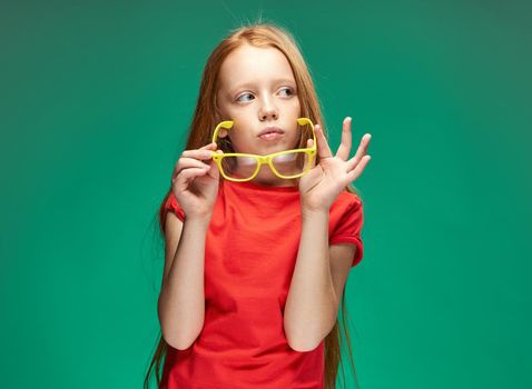 cheerful red-haired girl holding glasses in her hands learning school green background. High quality photo
