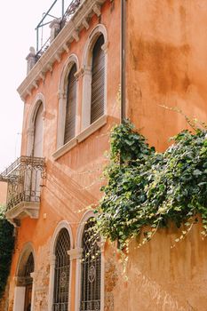 An ancient building in Venice, Italy, close-up. Peach-colored walls, classic Venetian arched windows with wooden closed rolls, a small balcony with a metal forged grille.