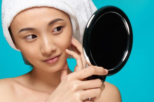 woman asian appearance naked shoulders mirror in hands clean skin hygiene blue background. High quality photo