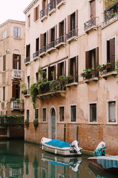 Boats moored at the walls of a building in canal in Venice, Italy. Classic Venetian street views - wooden shutters, brick houses, bridges