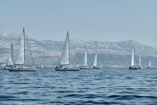 The race of sailboats, a regatta, reflection of sails on water, Intense competition, number of boat is on aft boats, island with windmills are on background
