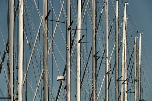 The number of masts of sailboats with the blue sky on a background, a sail regatta, reflection of masts on water, ropes and aluminum