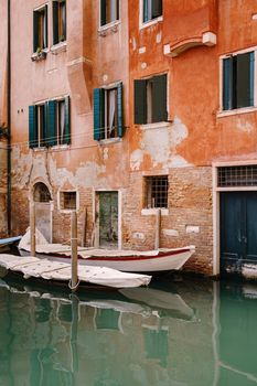 Boats moored at the walls of a building in canal in Venice, Italy. Classic Venetian street views - wooden shutters, brick houses, bridges