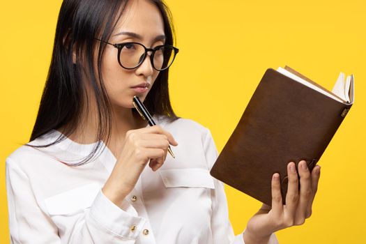 woman of asian appearance looking at notepad pen in hand an official yellow background. High quality photo