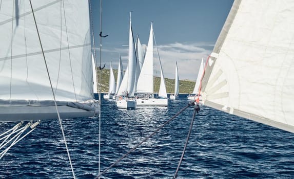 Sailboats compete in a sail regatta at sunset, race of sailboats, reflection of sails on water, multicolored spinnakers, number of boat is on aft boats, big white clouds is on background