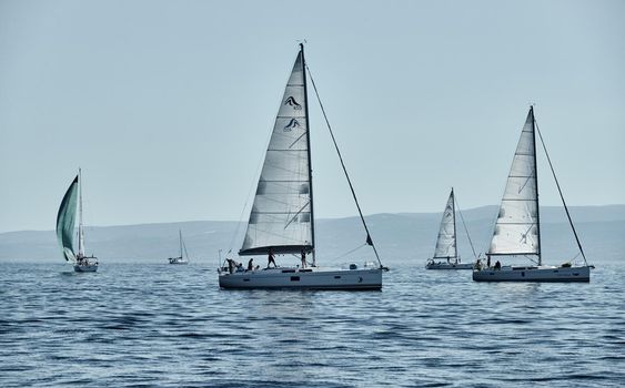 Croatia, Adriatic Sea, 15 September 2019: The race of sailboats, a regatta, reflection of sails on water, Intense competition, island with windmills are on background