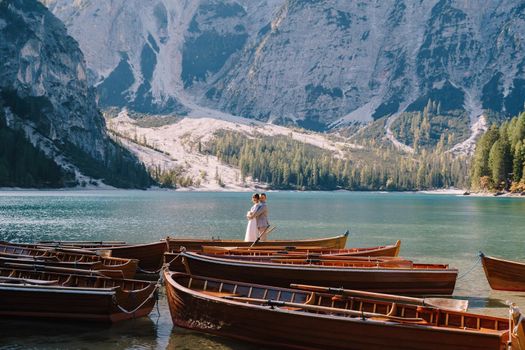 Bride and groom sailing in wooden boat, with oars at Lago di Braies lake in Italy. Wedding in Europe - Newlyweds are standing embracing in boat