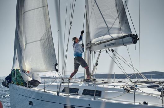 Croatia, Mediterranean Sea, 18 September 2019: The team of sailboat turns off the boat, sailboats compete in a sail regatta, The team works, pulls to a rope, the captain stands behind a steering wheel