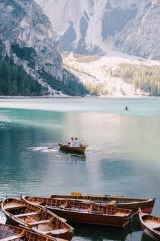 Wedding couple swim in a wooden boat on Lago di Braies in Italy. Newlyweds in Europe, at Braies Lake, in the Dolomites. The groom rows with oars, the bride sits opposite him.