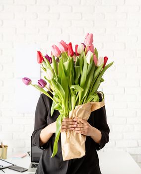 Small business concept. Portrait of young confident brunette business woman standing by the desk with fresh tulips bouquet