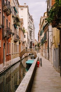Beautiful narrow canal in Venice, Italy. Small stone bridge connects houses from both sides of the canal. Building facades are aged by weather and water.