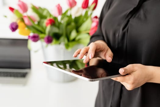 Small business concept. woman hands working on digital tablet, bucket of fresh tulips on background