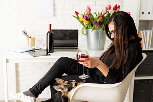 Small business concept. Young confident business woman drinking wine, celebrating holidays at home, having fun with her dog