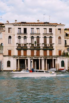 Tourists on the waterfront in Venice, against the background of the ancient facades of buildings standing in water. Water sightseeing in Venice, Italy.