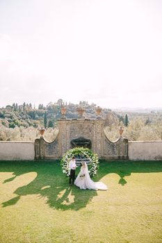 Wedding at an old winery villa in Tuscany, Italy. Wedding couple under a round arch of flowers. The groom reads out the wedding vows.