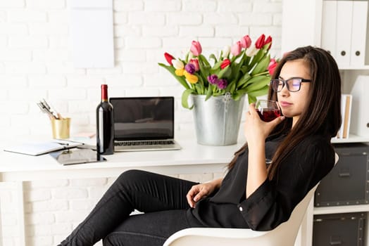 Small business concept. Young confident business woman drinking wine, celebrating spring holidays at the office
