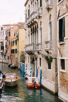 Boats moored at the walls of a building in canal in Venice, Italy. Classic Venetian street views - wooden shutters, brick houses, bridges