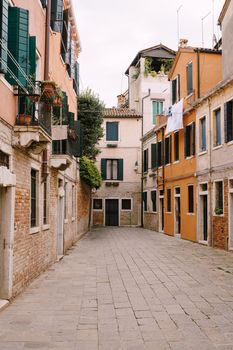 Dead end Venetian street. Five-story houses with blue-green wooden shutters on the windows, linen is dried in the windows, an old stone floor.