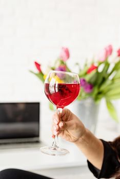 woman hand holding a glass of red wine celebrating spring holidays, bucket of tulips on background