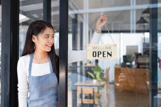 Small business owner smiling while turning the sign for the reopening of the place after the quarantine due to covid-19. Close up of woman  hands holding sign now we are open support local business.