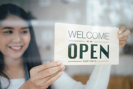 Small business owner smiling while turning the sign for the reopening of the place after the quarantine due to covid-19. Close up of woman  hands holding sign now we are open support local business.