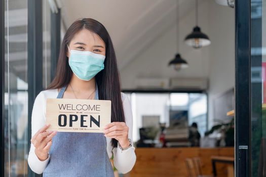 Reopen, Young Asia girl wear face mask turning a sign from closed to open sign after lockdown. 