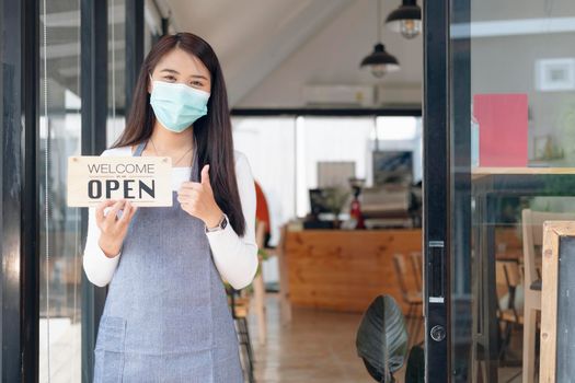 Reopen, Young Asia girl wear face mask turning a sign from closed to open sign after lockdown. 