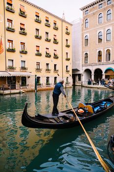 The gondolier rows a paddle in an empty gondola along the canal, against the backdrop of a yellow five-storey building.
