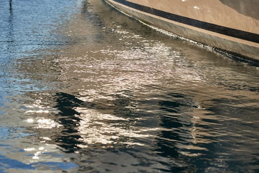 Board of the big boat of gold color, golden reflections of the sun on water at sunset, interesting texture, smooth lines