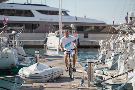 Croatia, Split, 15 September 2019: Brutal participant of a sailing regatta with boats on a background goes by bicycle on a pier, people is waiting for the forthcoming race