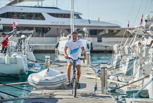 Croatia, Split, 15 September 2019: Brutal participant of a sailing regatta with boats on a background goes by bicycle on a pier, people is waiting for the forthcoming race