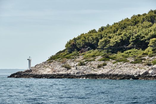 Small lighthouse on the island, Stone coast, sunny weather, green trees