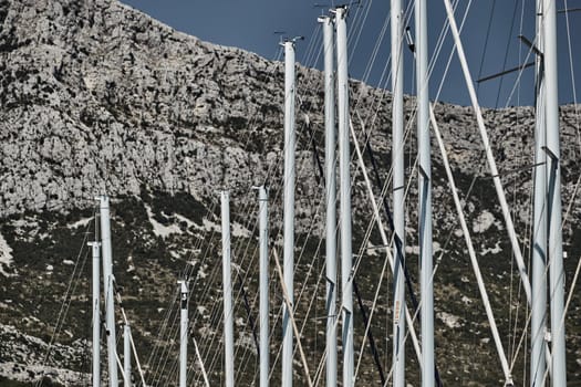 The number of masts of sailboats with the blue sky on a background, a sail regatta, reflection of masts on water, ropes and aluminum