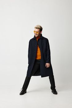 blond man in fashionable clothes spread his legs and light background orange sweater pants. High quality photo