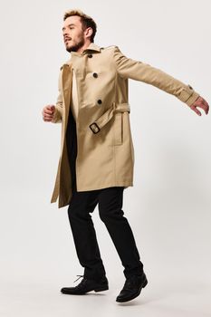 a guy in a beige coat gestures with his hands on a light background in full growth side view. High quality photo
