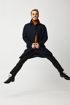 fashionable man in black coat jumped up with legs apart and orange sweater Copy Space. High quality photo