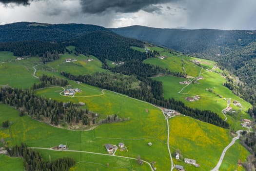 Aerial view of improbable green meadows of the Italian Alps, green slopes of the mountains, Bolzano, huge clouds over a valley, roof tops of houses, Dolomites on background, sunshines through clouds