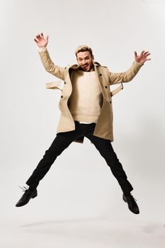 a successful man in a beige coat jumped up and gesticulates with his hands on a light background. High quality photo