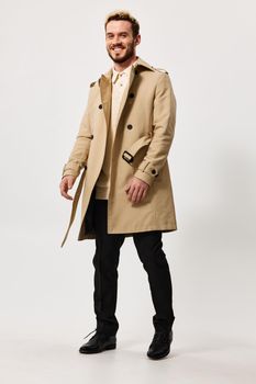 cute guy in beige coat and trousers goes to the side on a light background and fashion style suit. High quality photo