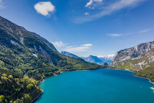 The Improbable aerial landscape of village Molveno, Italy, azure water of lake, empty beach, snow covered mountains Dolomites on background, roof top of chalet, sunny weather, a piers, coastline, slopes