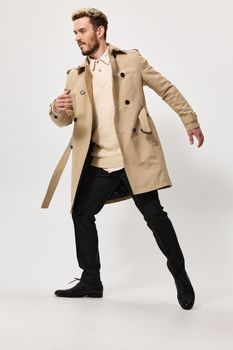 a man in a beige coat and trousers bent to the side and gesticulates with his hands on a light background. High quality photo