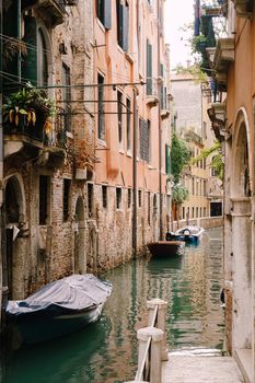 Boats moored at the walls of a building in canal in Venice, Italy. Classic Venetian street views - wooden shutters, brick houses, bridges